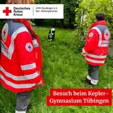 Zwei Einsatzkräfte stehen auf der Wiese, ein Border Collie läuft auf sie zu
