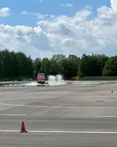 Trainingsplatz für Fahrzeuge mit nasser Fahrbahn und Wasserfontainen und ein Dienstwagen des DRK fährt