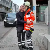 Einsatzkraft umarmt Schaufensterpuppe die auch die Einsatzjacke und Ausrüstung des DRK trägtq