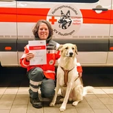 Rettungshundeteam nach der Prüfung mit der Urkunde vor einem Einsatzwagen