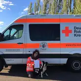 Rettungshundeteam kniet mit Urkunde vor einem Einsatzwagen