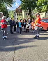 Eine gruppe Kinder des JRK Plochingen mit ein paar Einsatzkräften der Rettungshunde mit einem Mantrailer Hund in der Mitte auf der Straße