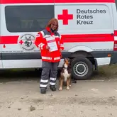 Rettungshundeteam Mensch und Hund stehen mit Urkunde vor Einsatzfahrzeug
