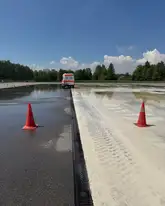 Auf einem Trainingsplatz eine nasse Fahrbahn mit zwei Verkehrskegel und einem einsatzwagen des DRK