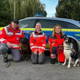 Mantrailteams des DRK vor einem Poilizeifahrzeug nach einem Einsatz