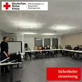 Personen in einem Raum an Tischen bei einem Vortrag