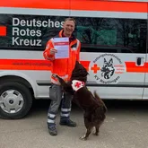 Till und Frieder Rettungshundeteam mit Urkunde vor Einsatzwagen