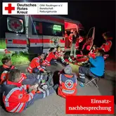 Einsatzkräfte sitzen bei Nacht vor einem Einsatzfahrzeug auf dem Boden und Besprechen den Einsatz